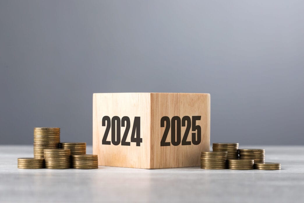 Wooden blocks transitioning from 2024 to 2025, accompanied by neatly stacked coins, symbolizing financial growth and preparation for the upcoming year | Meridian Source