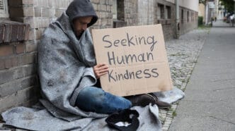 Male,Beggar,In,Hood,Showing,Seeking,Human,Kindness,Sign,On | Meridian Source