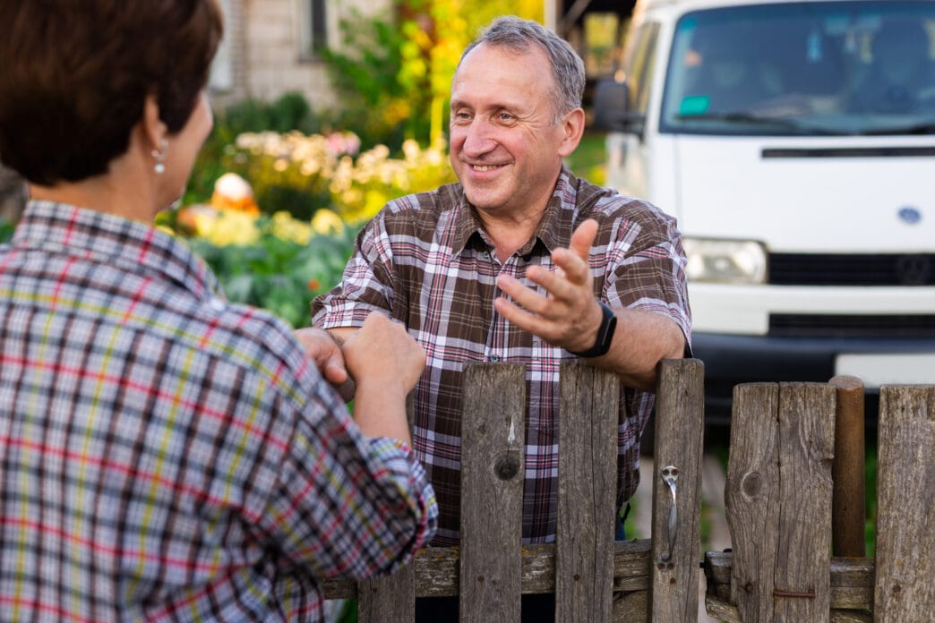 neighbors man and woman chatting near the fence in the village | Meridian Source