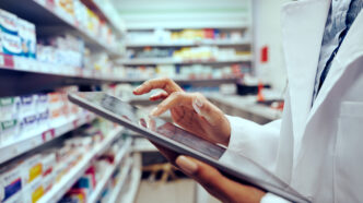 Closeup of hands of young female pharmacist checking inventory in medical store using digital tablet | Meridian Source