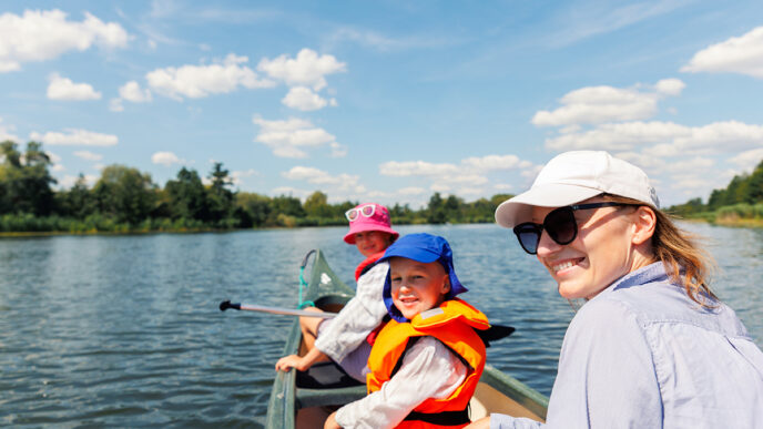 Woman two children enjoy having fun paddling canoe rent across lake river water wearing bright orange life vests hot sunny summer day Healthy recreational activity lifestyle vacation trip journey | Meridian Source