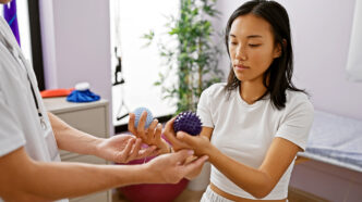 A woman patient examines rehabilitation equipment with a therapist in a clinics treatment room | Meridian Source