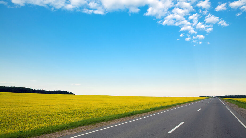 Never ending highway through green fields and blue cloudy sky | Meridian Source