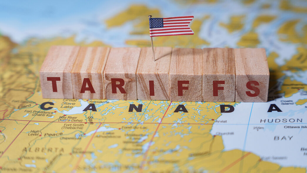 Wooden blocks spelling TARIFFS with a small US flag on top placed on a map highlighting Canada symbolizing trade policies and economic relations | Meridian Source